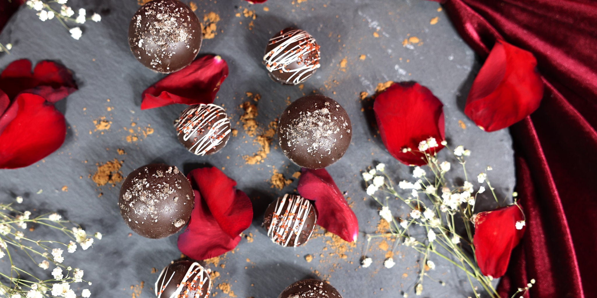 Chocolate truffles with red roses and white flowers on a dark surface